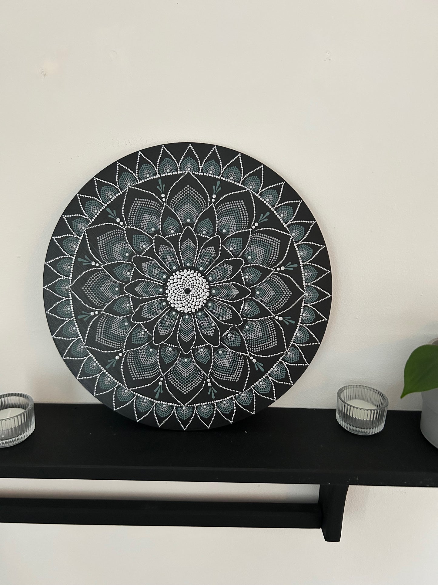 Decorative black mandala wall art on a white wall with a black shelf below.