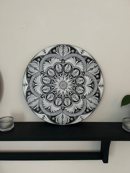 Decorative black and white mandala plate on a shelf against a white wall