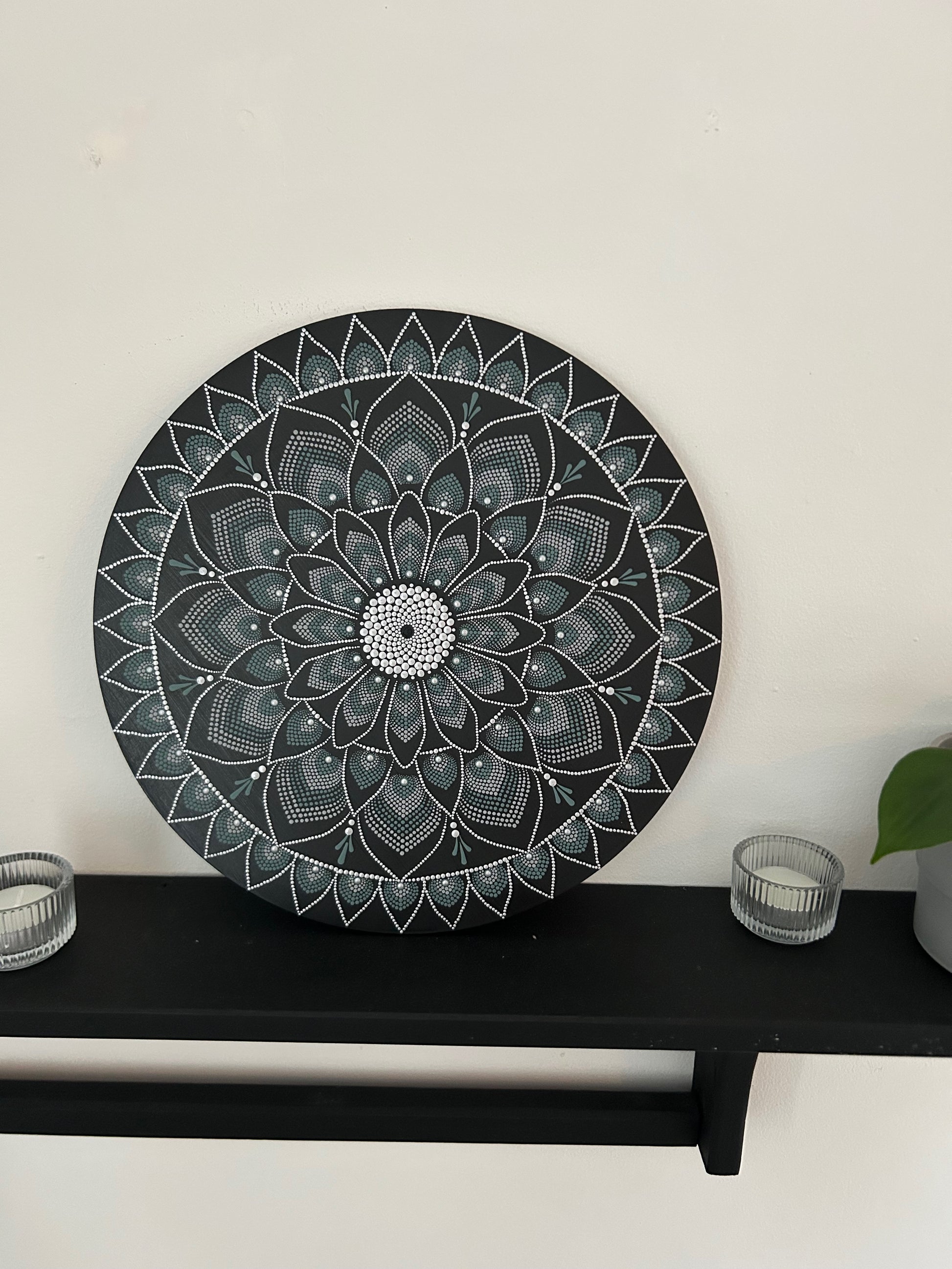 Decorative black mandala wall art on a white wall with a black shelf below.